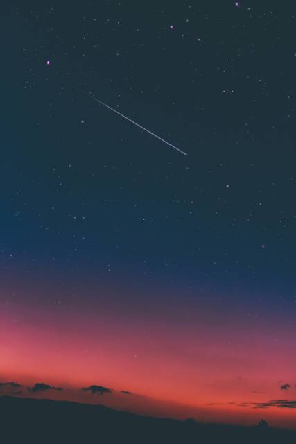 Shooting star streaking across twilight sky with pink and blue gradient