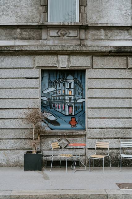 Urban street art mural on weathered building facade with chairs in front