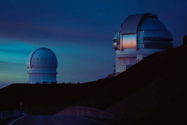 Observatory domes on a hilltop at twilight with colorful sky