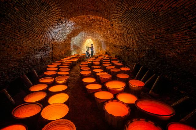 Illuminated wine barrels in a brick cellar tunnel creating dramatic atmosphere
