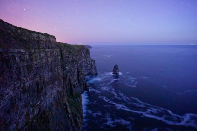 Dramatic coastal cliffs at twilight with sea stack formation and purple sky