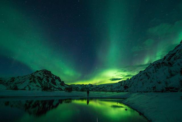 Northern lights aurora borealis glowing green over snowy mountains and frozen lake