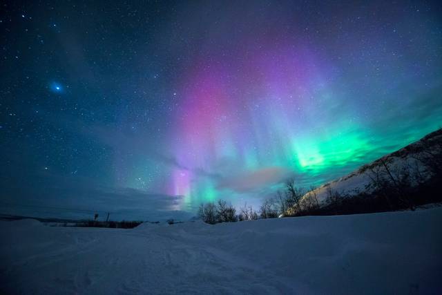 Colorful aurora borealis with pink and green lights over snowy landscape
